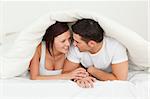 Happy couple hiding under a blanket in a bedroom