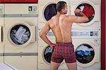 Muscular man in boxer shorts looks at wristwatch in laundromat