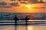 Silhouettes of three surfers at red sunset. Kuta beach. Bali