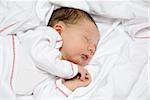 A young baby is sleeping on a white bed with a blanket.