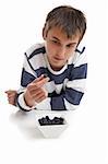 A boy looking intensely at a blueberry held between two fingers.