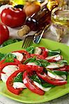 Salad caprese with fresh tomatoes, basil and cheese on a green plate.