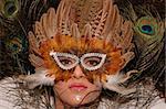 Girl wearing makeup made of rhinestone flowers with peacock feathers in her hair and mask in her face