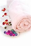 Pink rolled up towel with bath beads on white background