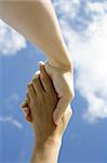 A pair of hands holding or shaking each other against a blue sky. Concept: Agreeement reached or helping hand.