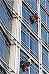 Two window washers descend on ropes high above the city. The building is a very modern glass structure.