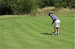 Golfer putting on the green. Ball and golf club are in slight movement.