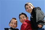 Three boys smiling with a blue sky background