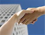 A pair of hands holding or shaking each other against a building background. Concept: Business deal done.