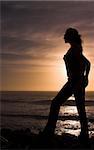 Silhouette of a blonde woman with long hair at sunset by the ocean.