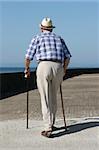 Rear view of an elderly man walking with walking sticks on a beach promenade.