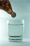 A hand dropping aspirin tablet into glass with water.