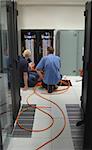 Three electricians install additional power cables into the distribution board within a data centre.