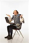 William Shakespeare in period clothing sitting in school desk with laptop and shrugging at viewer.