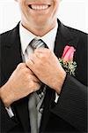 Close up of Caucasian groom adjusting his tie.