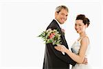 Portrait of Caucasian groom and Asian bride embracing.