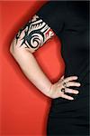 Caucasian woman's tattooed arm with hand on hip against red background.