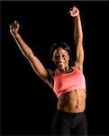 Smiling African American young adult woman in sports bra stretching arms above head.