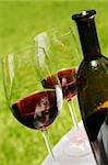 Red wine in glasses with bottle and green outdoor background