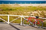 Red beach cruiser bicycle leaning against walkway rail on beach on Bald Head Island, North Carolina.