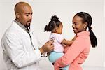 African-American male pediatrician examining baby girl being held by mother.