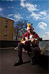 Portrait of a mid-adult Caucasian male punk  sitting on a skylight playing guitar.