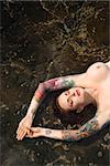 Sexy nude tattooed Caucasian woman lying in tidal pool in Maui, Hawaii, USA.