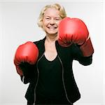 Caucasian senior woman wearing boxing gloves and throwing punch at viewer.