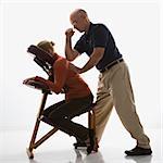 Caucasian middle-aged male massage therapist massaging back of Caucasian middle-aged woman sitting in massage chair with his elbow.