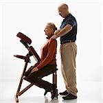 Caucasian middle-aged male massage therapist massaging shoulders of Caucasian middle-aged woman sitting in massage chair.