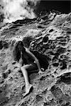 Young Asian nude woman sitting in a crevice in a rock.