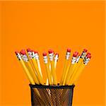 Group of pencils in pencil holder on orange background.