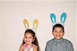 Hispanic boy and girl wearing bunny ears smiling and looking at viewer.