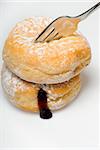 two jelly donuts being cut by fork with jelly leaking out