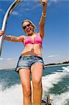 A stunningly beautiful and wealthy young blond woman holding on to the back of a powerboat and having fun