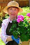 Attractive senior woman holding a pot with flowers in her garden
