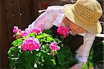 Senior woman with a pot of geranuim flowers in her garden, focus on flowers