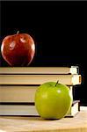 A red and green apple with school textbooks on black background