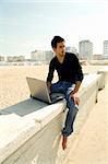 Attractive young man working with a laptop sitting outdoor near the ocean