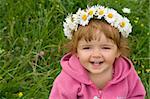 Baby girl with daisy wreath looking up and laughing on the spring meadow full of flowers
