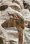 A rock climber works his way over an overhang. He is hanging onto the nose of the problem.