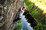 A female climber on a steep rock face looking for the next hold.  Shallow depth of field is used to isolate the climber.