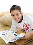 Boy in a room reading a book over a carpet. He is smiling and looks amused. Visit my gallery for more images of children