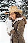 Caucasian young adult female wearing straw cowboy hat outdoors in snow holding coffee cup and smililng at viewer.