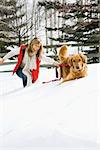 Attractive smiling mid adult Caucasian blond woman being pulled through the snow by a Golden Retriever.