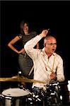 drummer playing over black backdrop with woman standing in background