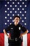 Portrait of mid adult Caucasian policewoman standing with hands on holster and American flag as backdrop smiling at viewer.