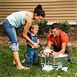 Caucasian family with toddler son washing English Bulldog in backyard.