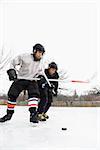 Two boys in ice hockey uniforms playing hockey on ice rink.