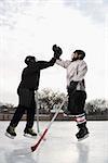 Two boys in ice hockey uniforms giving eachother high five on ice rink.